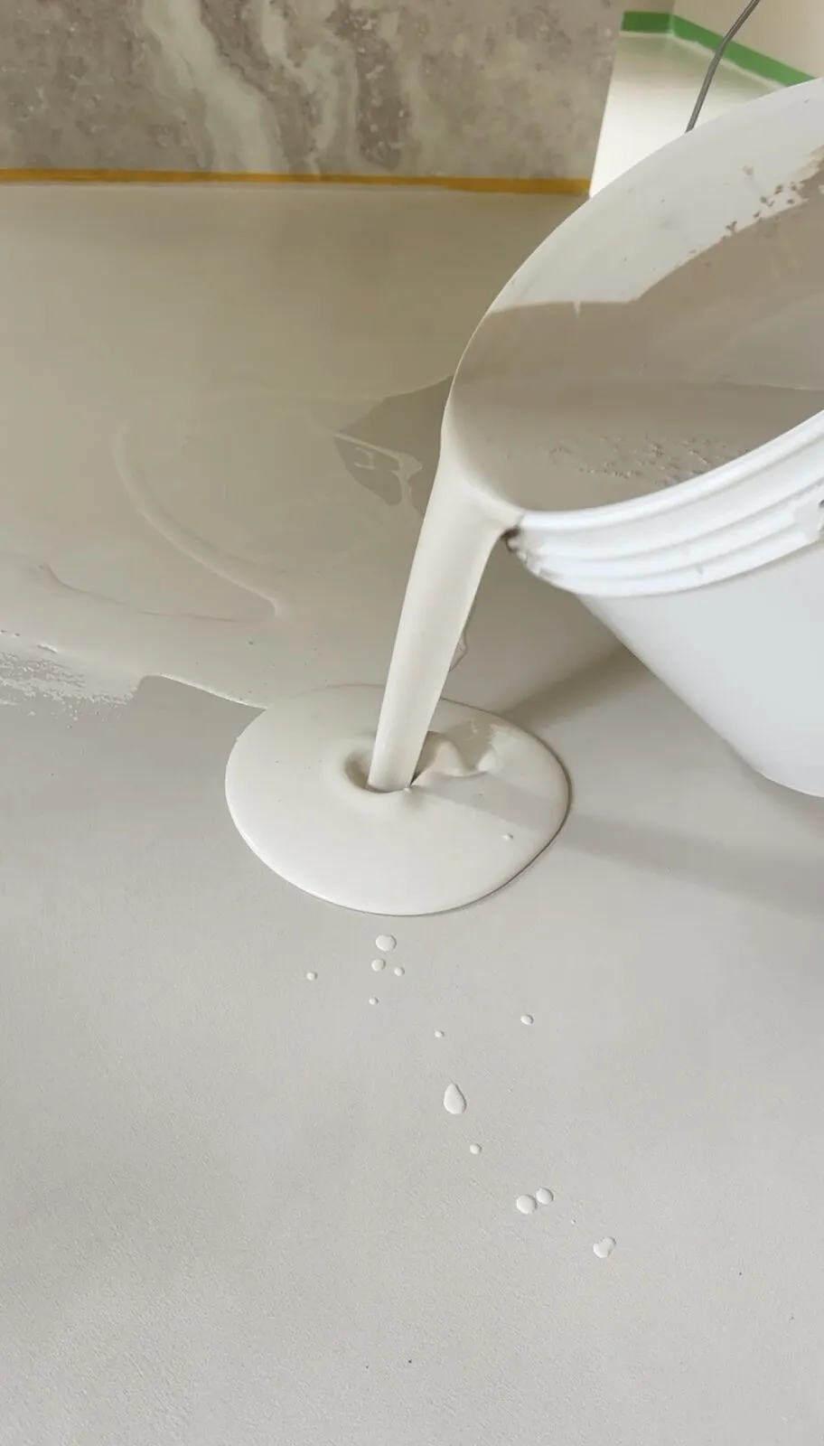 Microcement wordt uit de emmer op de badkamervloer gegoten en met de hand uitgesmeerd