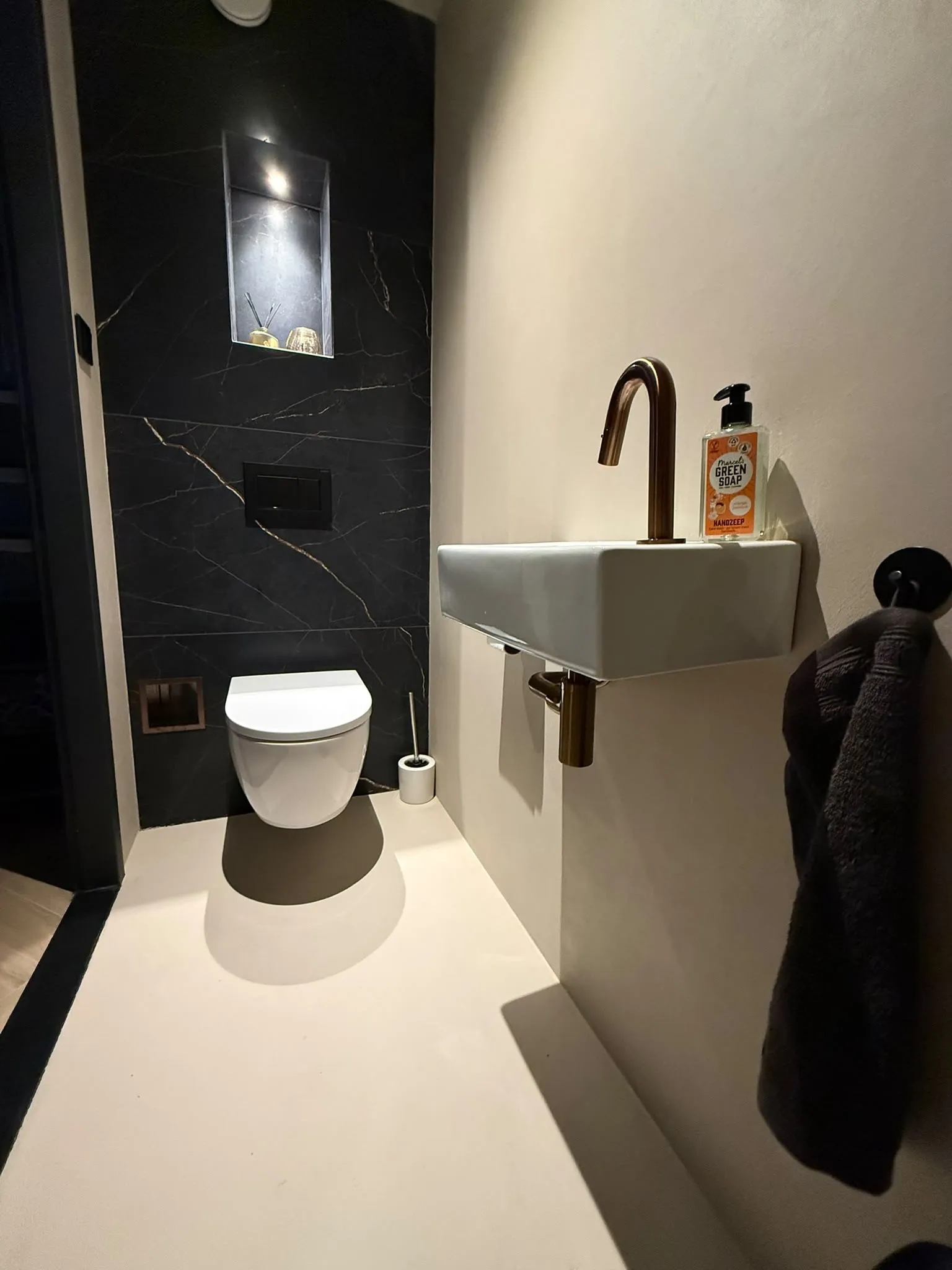 Toilet met een naadloze vloer in microcement en een koperen kraan