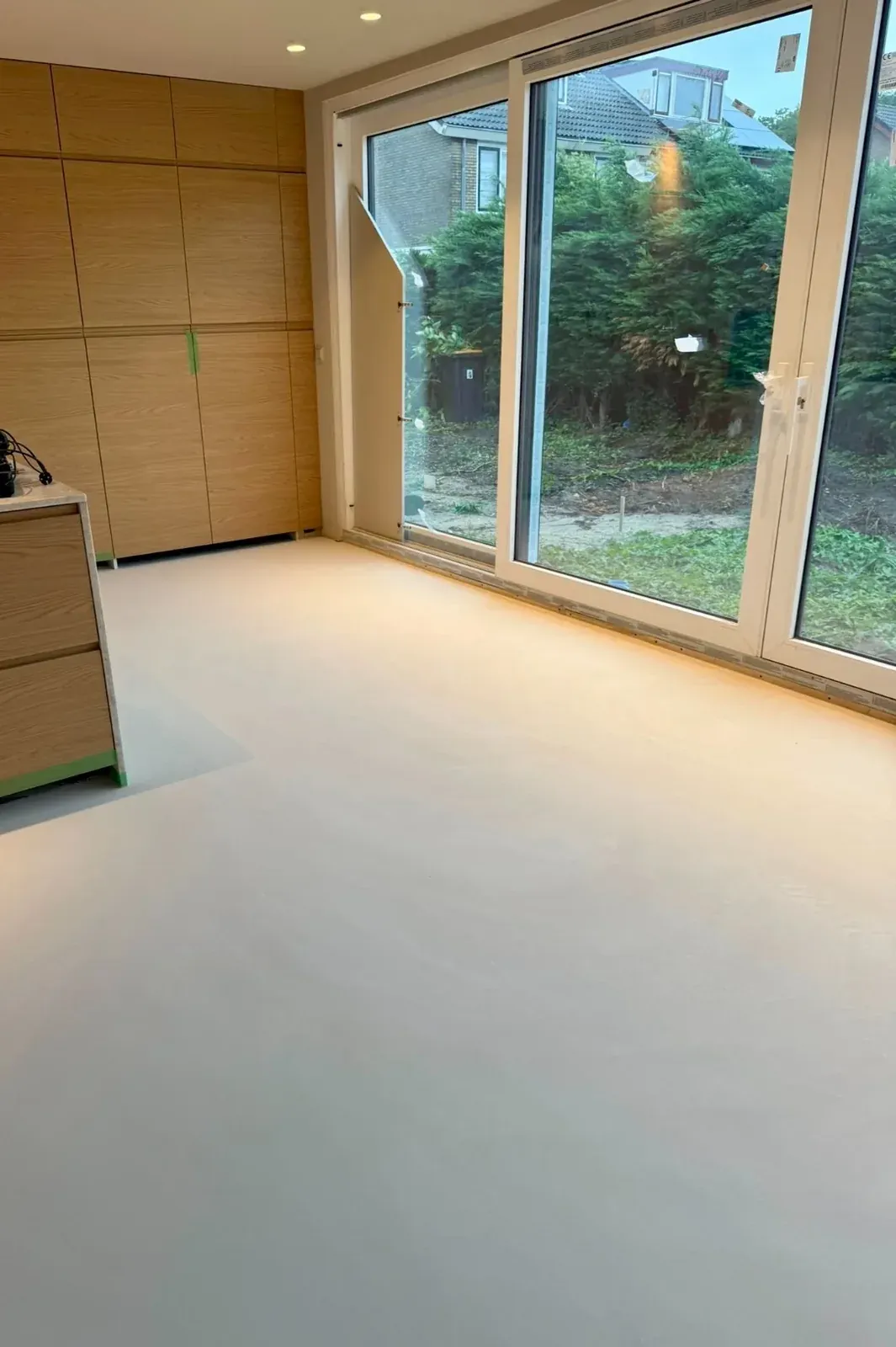 Lichte naadloze lavasteen gietvloer in een woonkamer met houten keuken en brede glazen pui