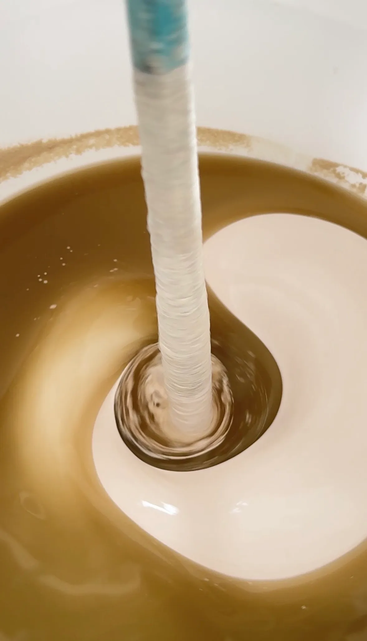 Pigment wordt met de mixer door het witte microcement gedraaid, halverwege zie je nog twee kleuren naast elkaar.