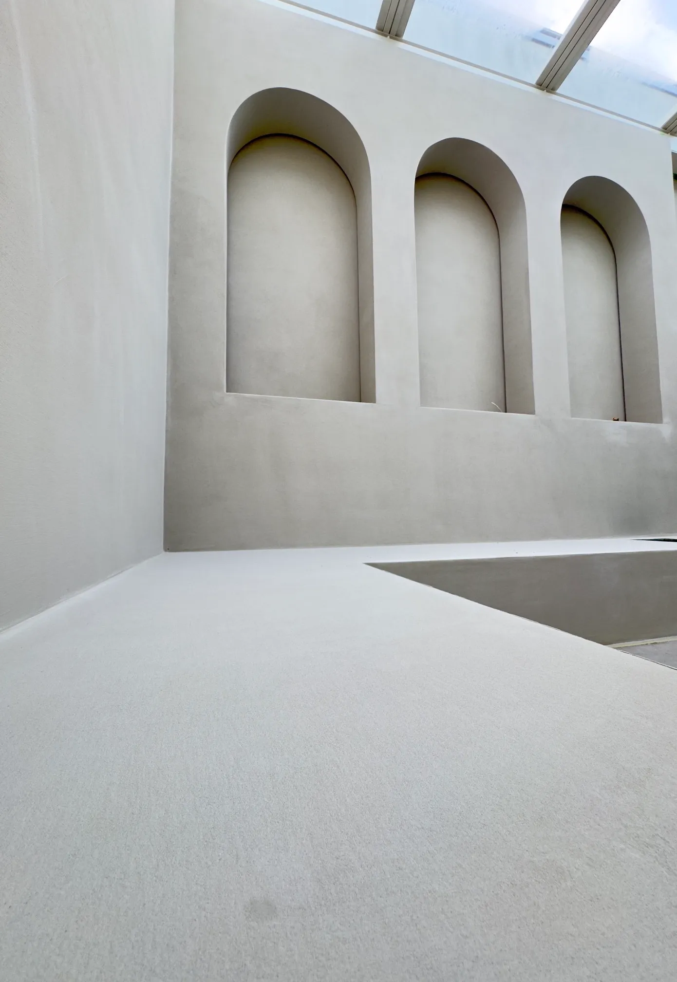 Patio van een penthouse in Rotterdam, dichtgemaakt met een glazen pui: wand met drie boognissen in microcement, mat en naadloos