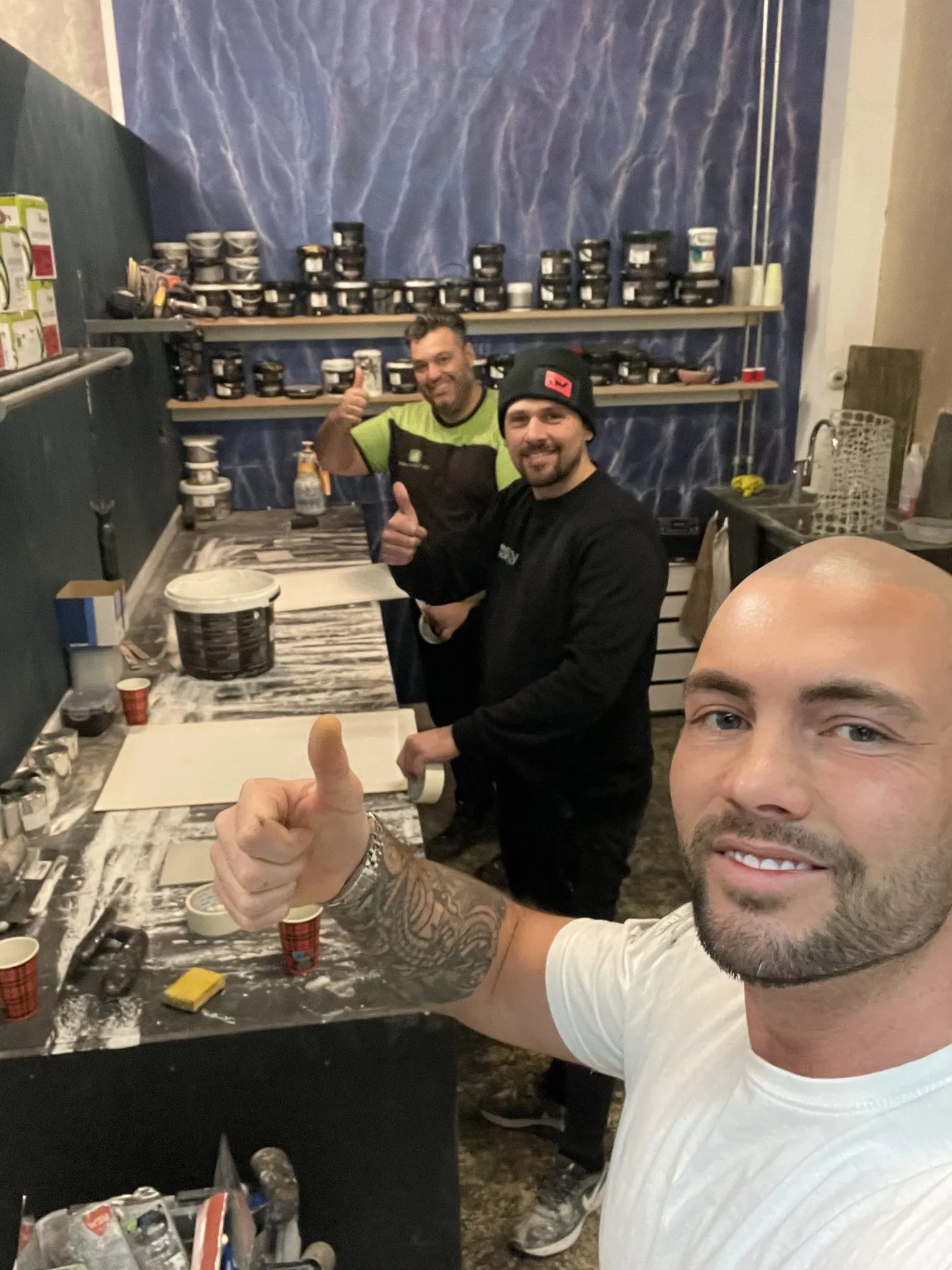Tim aan de werktafel met cursisten, achter hen planken vol potten stucwerk